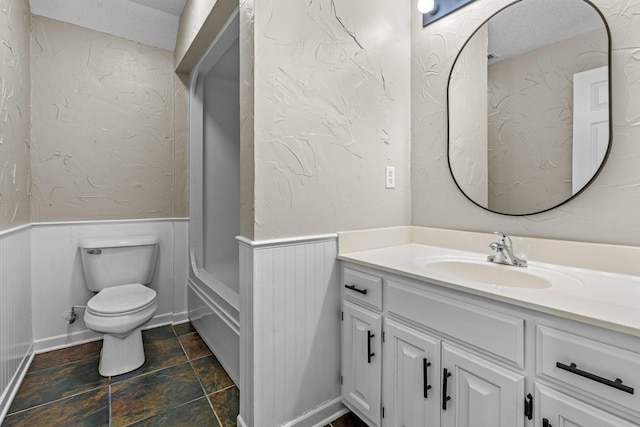 full bathroom with a textured wall, toilet, wainscoting, vanity, and a textured ceiling