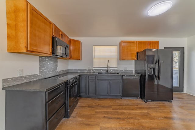 kitchen featuring dark countertops, brown cabinetry, a sink, wood finished floors, and black appliances