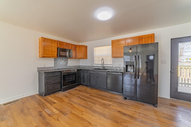 kitchen featuring wood finished floors, a sink, visible vents, black appliances, and dark countertops