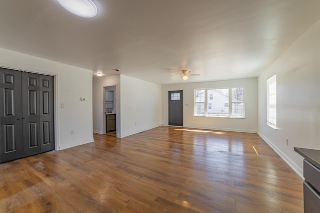 unfurnished living room with dark wood-style flooring, ceiling fan, and baseboards