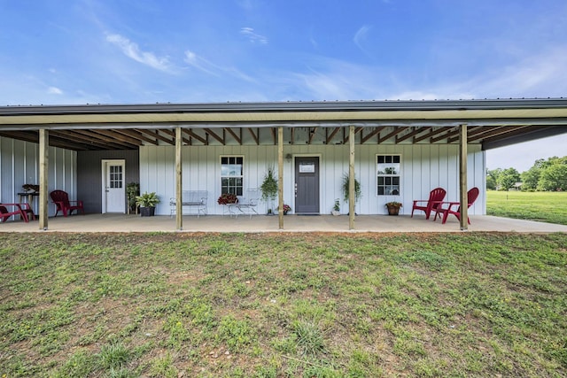 rear view of property with board and batten siding, a patio area, and a yard