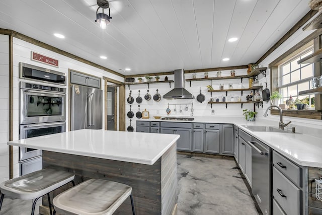 kitchen featuring open shelves, stainless steel appliances, gray cabinets, a sink, and wall chimney range hood