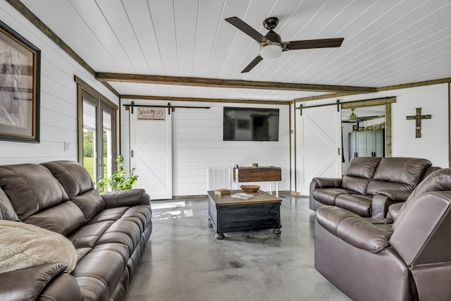 living room with a barn door, wooden walls, ceiling fan, beamed ceiling, and concrete flooring