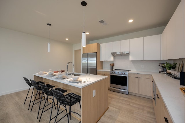 kitchen with stainless steel appliances, a sink, light wood-type flooring, under cabinet range hood, and a kitchen bar