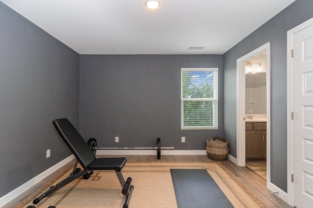 exercise room featuring light wood-type flooring, visible vents, a sink, and baseboards