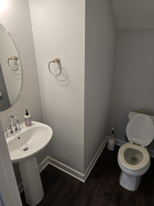 half bathroom featuring a sink, wood finished floors, toilet, and baseboards