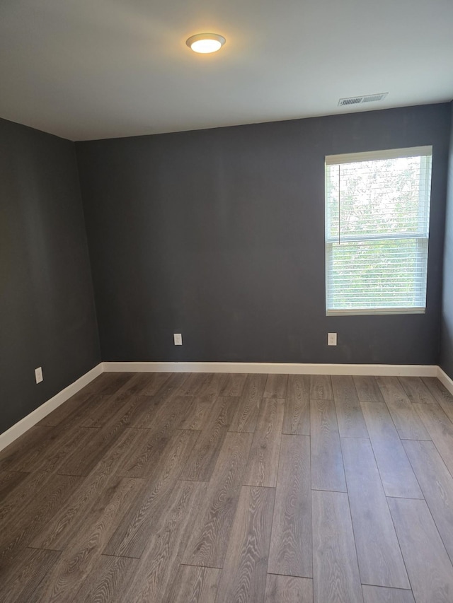 empty room featuring visible vents, dark wood finished floors, and baseboards