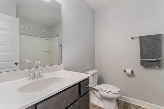 bathroom with a shower, toilet, vanity, wood finished floors, and baseboards