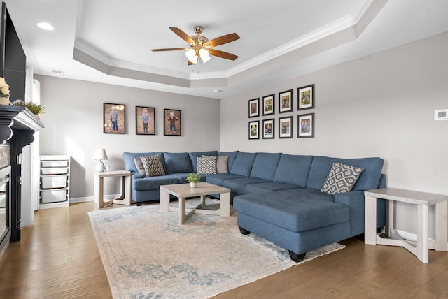 living room featuring a tray ceiling, a glass covered fireplace, crown molding, and wood finished floors