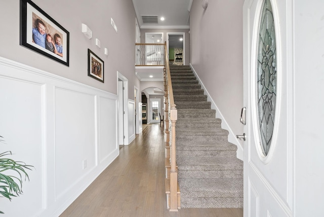 entrance foyer featuring visible vents, arched walkways, wood finished floors, crown molding, and a decorative wall