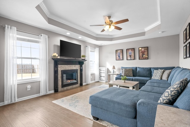 living area featuring wood finished floors, baseboards, a tiled fireplace, a raised ceiling, and crown molding