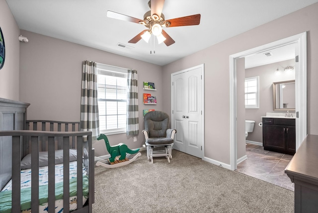 carpeted bedroom featuring a sink, a ceiling fan, visible vents, baseboards, and ensuite bath