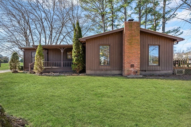 view of front of house with board and batten siding, a sunroom, a chimney, and a front lawn