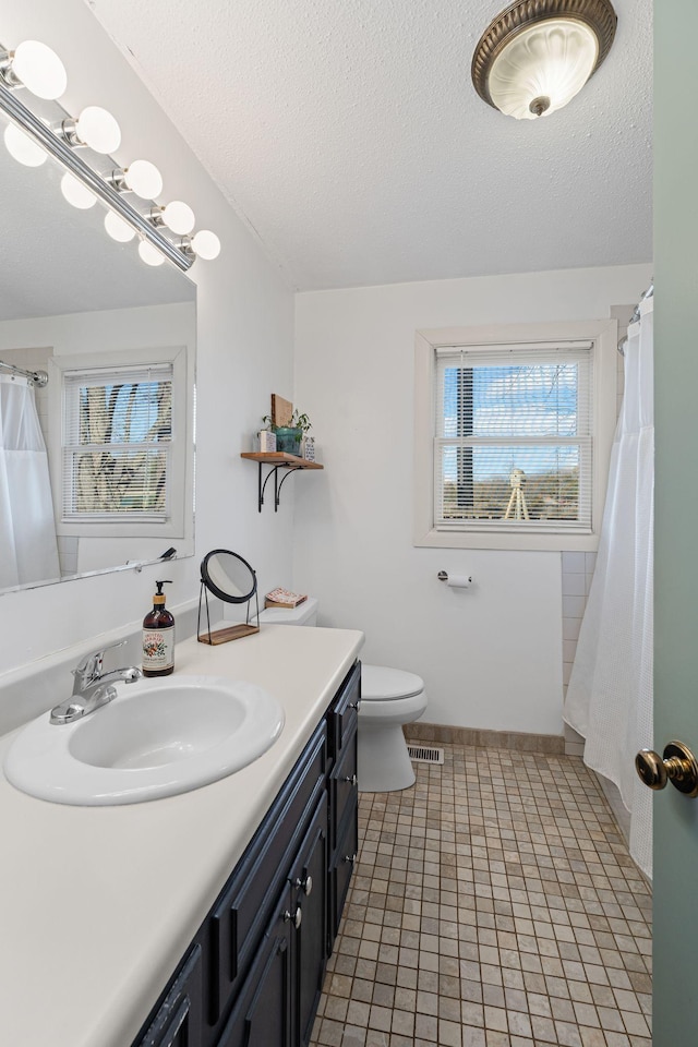 bathroom featuring a textured ceiling, toilet, vanity, and visible vents