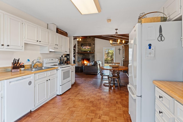 kitchen featuring a stone fireplace, ceiling fan with notable chandelier, white appliances, a sink, and white cabinetry