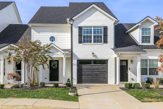 traditional home featuring an attached garage, brick siding, concrete driveway, and roof with shingles