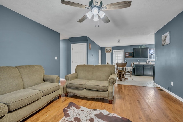 living area with a ceiling fan, baseboards, visible vents, and light wood finished floors