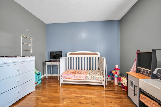 bedroom with a nursery area, wood finished floors, and baseboards