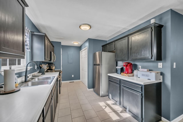 kitchen with light tile patterned floors, baseboards, appliances with stainless steel finishes, light countertops, and a sink