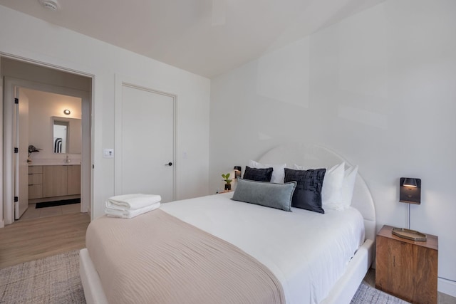 bedroom with ensuite bathroom and light wood-style flooring