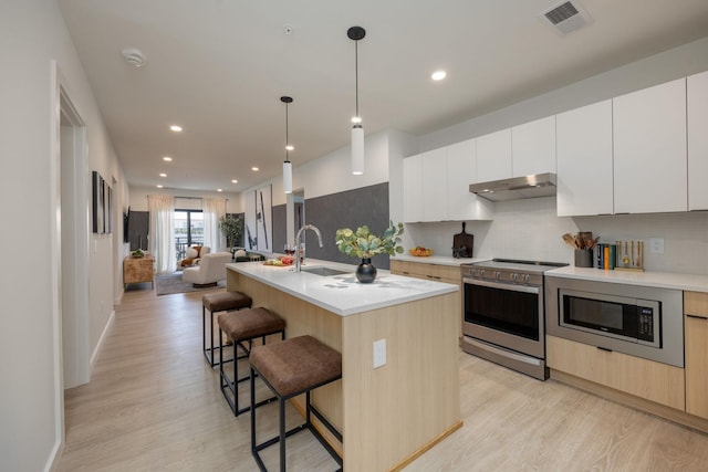 kitchen featuring a sink, visible vents, open floor plan, appliances with stainless steel finishes, and a kitchen bar