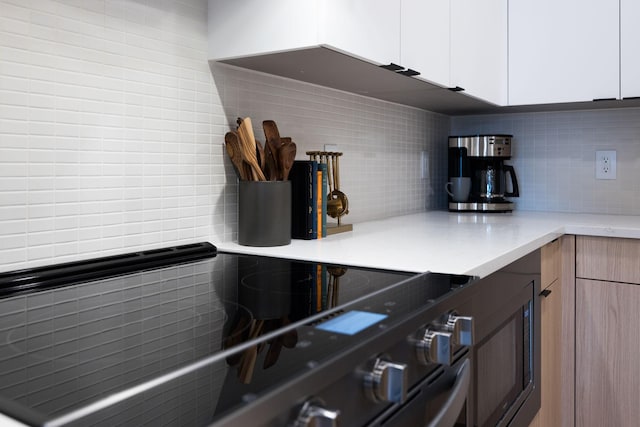 kitchen with black electric range, white cabinetry, and backsplash