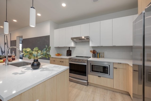 kitchen with modern cabinets, appliances with stainless steel finishes, light stone counters, under cabinet range hood, and a sink