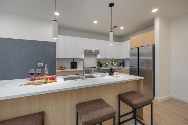 kitchen with freestanding refrigerator, a sink, under cabinet range hood, and a kitchen breakfast bar