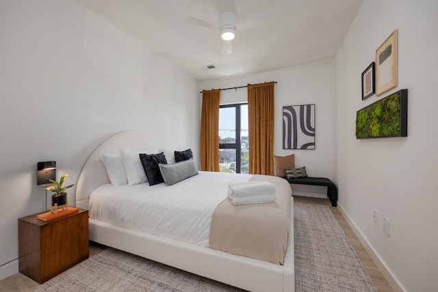 bedroom with a ceiling fan, visible vents, baseboards, and wood finished floors