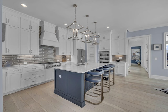 kitchen with custom range hood, appliances with stainless steel finishes, light countertops, white cabinetry, and a sink