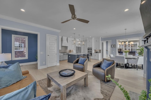 living area featuring recessed lighting, crown molding, light wood-style flooring, and ceiling fan with notable chandelier