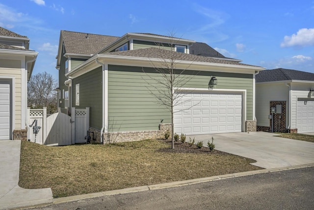 view of side of property with brick siding, a shingled roof, concrete driveway, a gate, and a garage