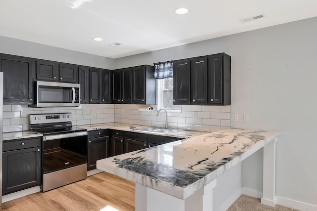 kitchen with visible vents, appliances with stainless steel finishes, a peninsula, dark cabinetry, and a sink