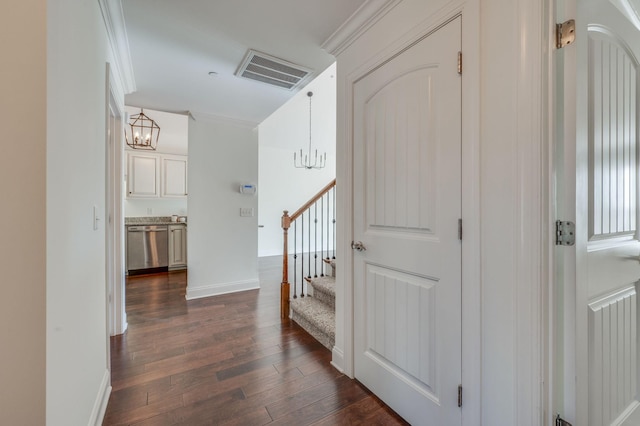 hallway featuring visible vents, ornamental molding, dark wood-style flooring, stairs, and a notable chandelier