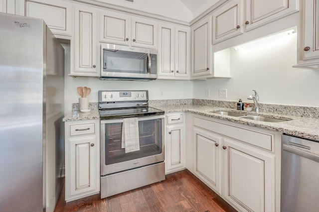 kitchen featuring appliances with stainless steel finishes, dark wood-type flooring, a sink, and light stone countertops