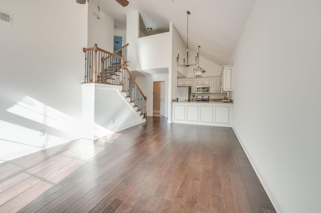 unfurnished living room featuring visible vents, dark wood-type flooring, ceiling fan, high vaulted ceiling, and stairs