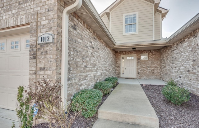 doorway to property featuring a garage and brick siding