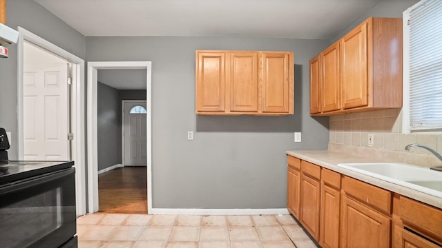 kitchen with light countertops, backsplash, electric range, a sink, and baseboards