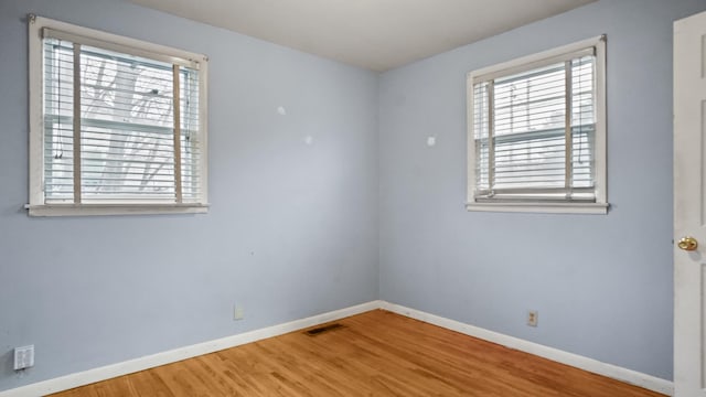 spare room featuring baseboards, visible vents, and wood finished floors