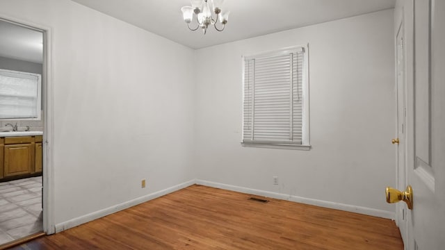 spare room with visible vents, light wood-style flooring, a sink, a chandelier, and baseboards