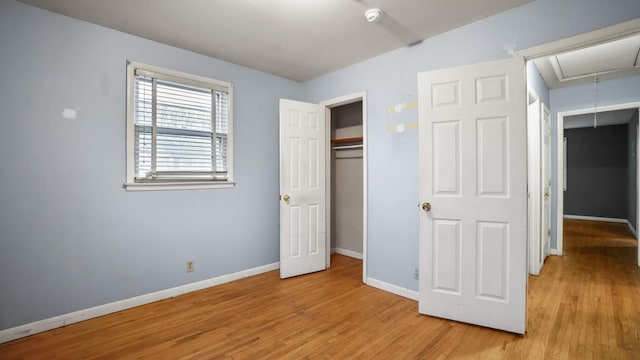 unfurnished bedroom with light wood finished floors, attic access, baseboards, and a closet