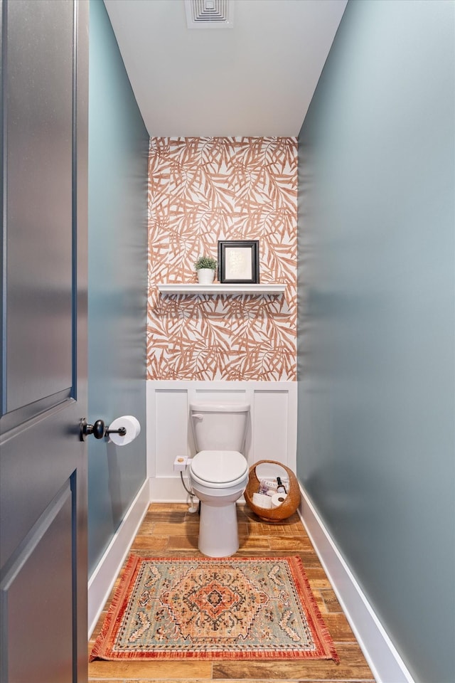 bathroom with wallpapered walls, baseboards, toilet, an accent wall, and wood finished floors