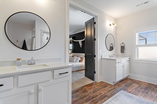 ensuite bathroom with wood finished floors, two vanities, a sink, and visible vents