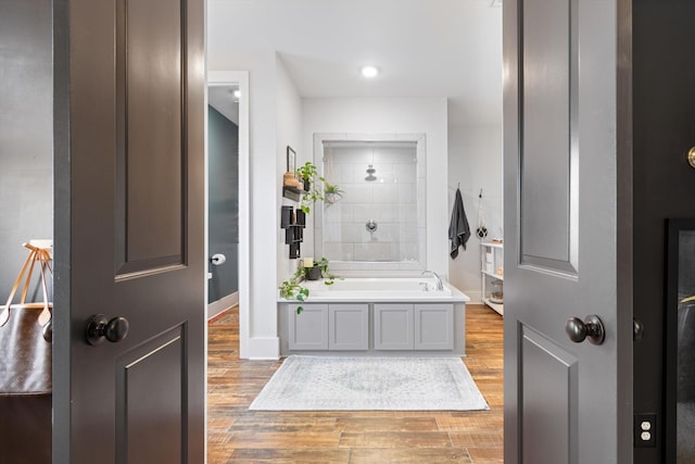 bathroom with a bath, baseboards, wood finished floors, and tiled shower