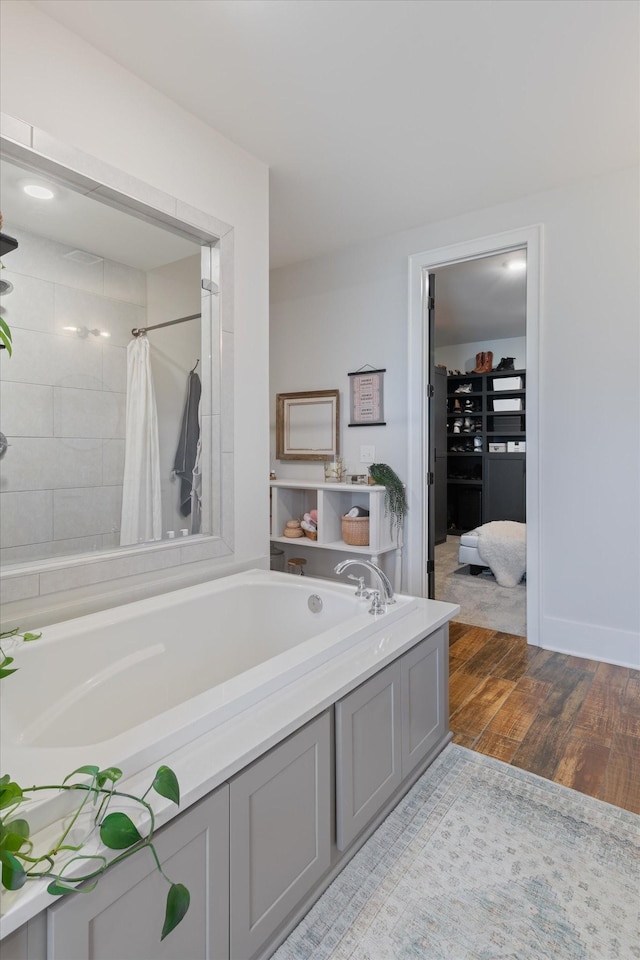 bathroom with baseboards, a washtub, a tile shower, and wood finished floors