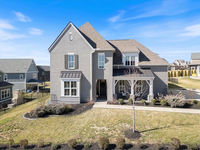 view of front of house with roof with shingles, brick siding, a standing seam roof, fence, and a front lawn