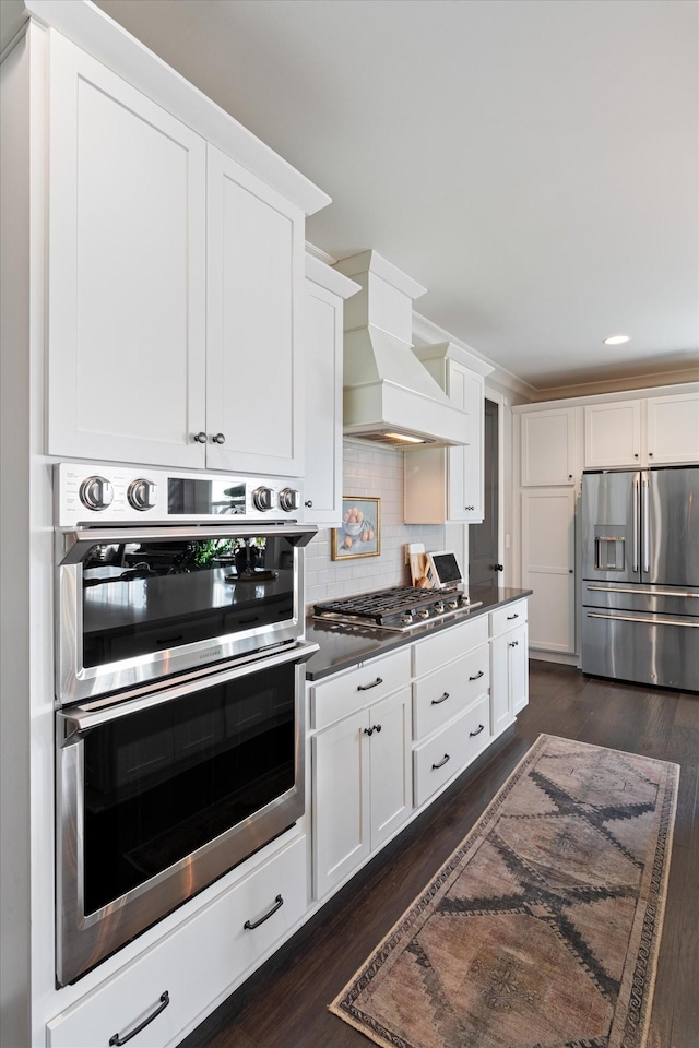 kitchen featuring dark wood finished floors, custom exhaust hood, stainless steel appliances, dark countertops, and white cabinets