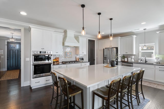 kitchen featuring stainless steel appliances, a sink, custom exhaust hood, a center island, and crown molding