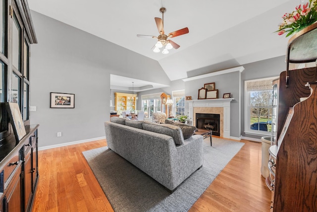 living area featuring a tile fireplace, baseboards, lofted ceiling, and light wood finished floors