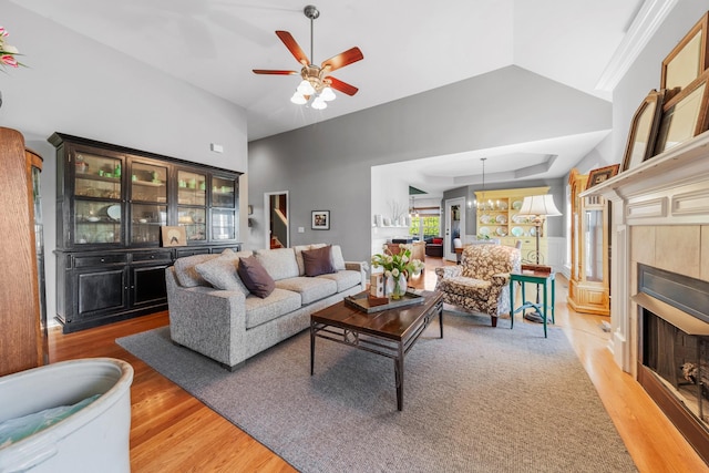 living area with lofted ceiling, light wood-type flooring, a tiled fireplace, and a ceiling fan